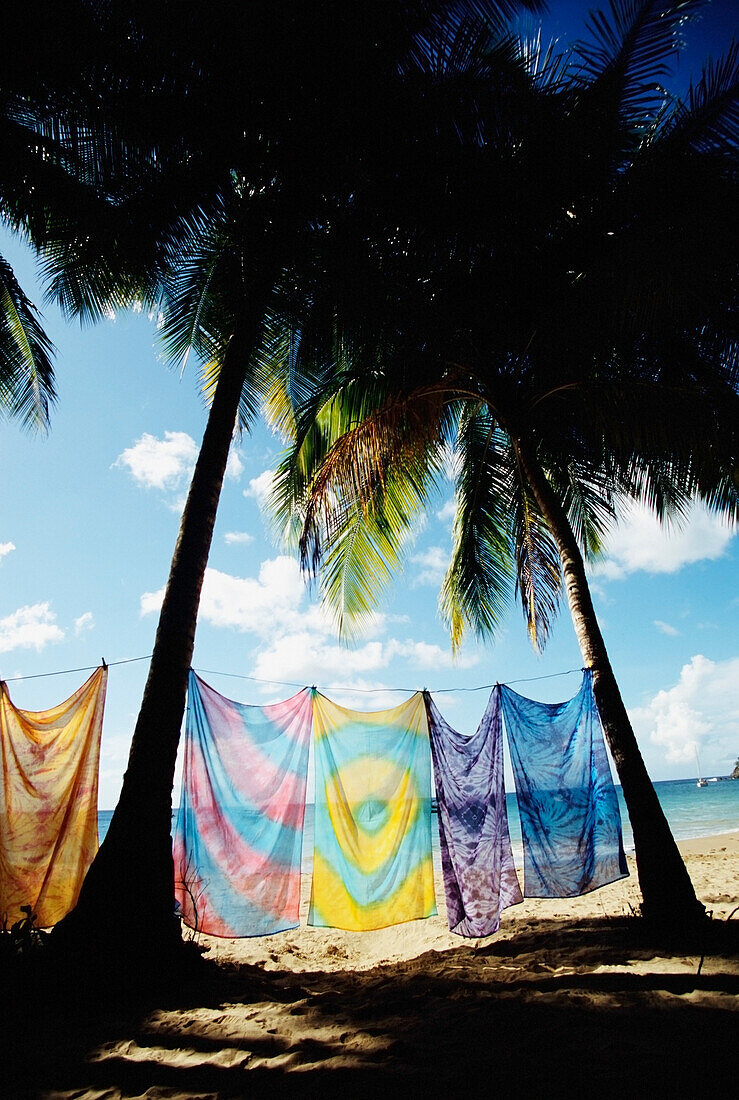 Sarongs hängen an einer Wäscheleine zwischen zwei Palmen am Strand