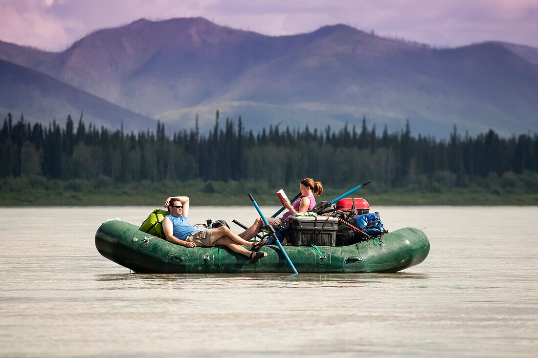 A Couple Enjoys The Day With Reading A Book And Napping On A Yukon River Raft Float Trip In Yukon Charley-Rivers National Preserve, Interior Alaska, Summer