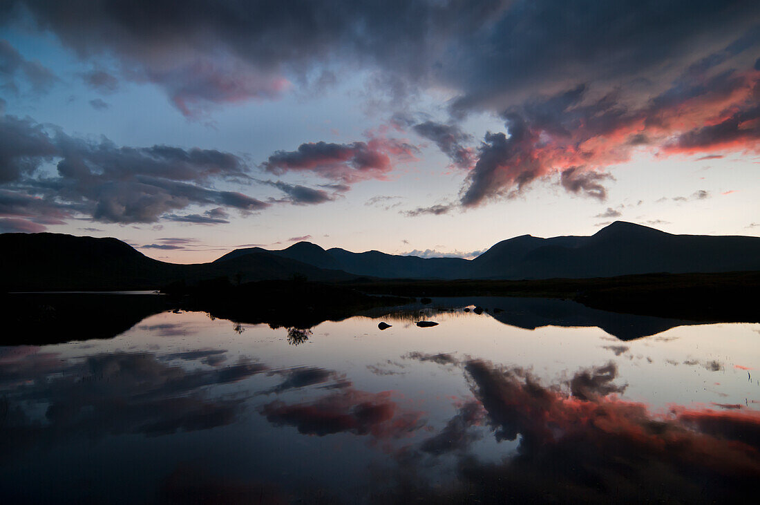 Spiegelbild von schemenhaften Bergen und Wolken bei Sonnenuntergang in einem See; Rannoch Moor, Schottland