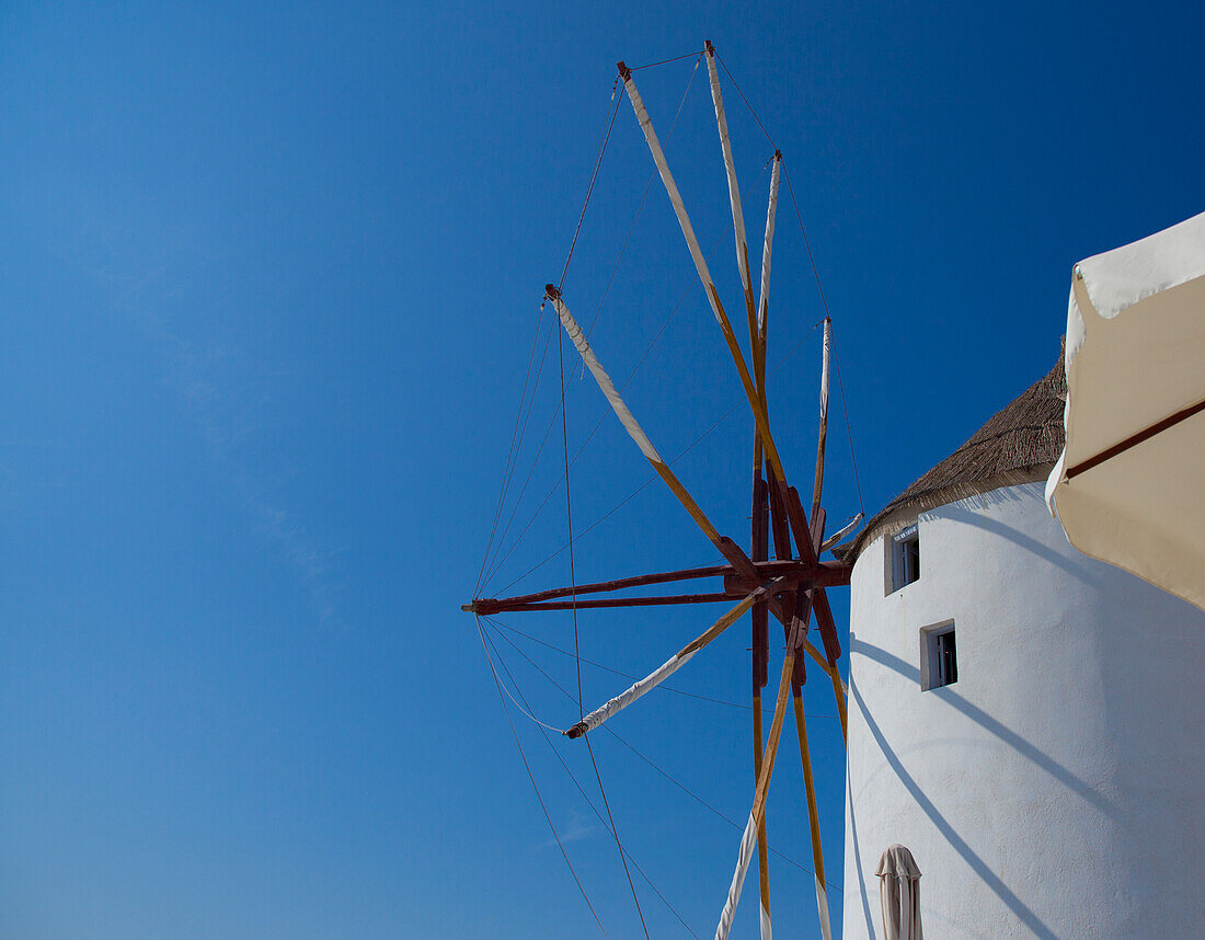 Windmill and a white building against a blue sky; Oia greece
