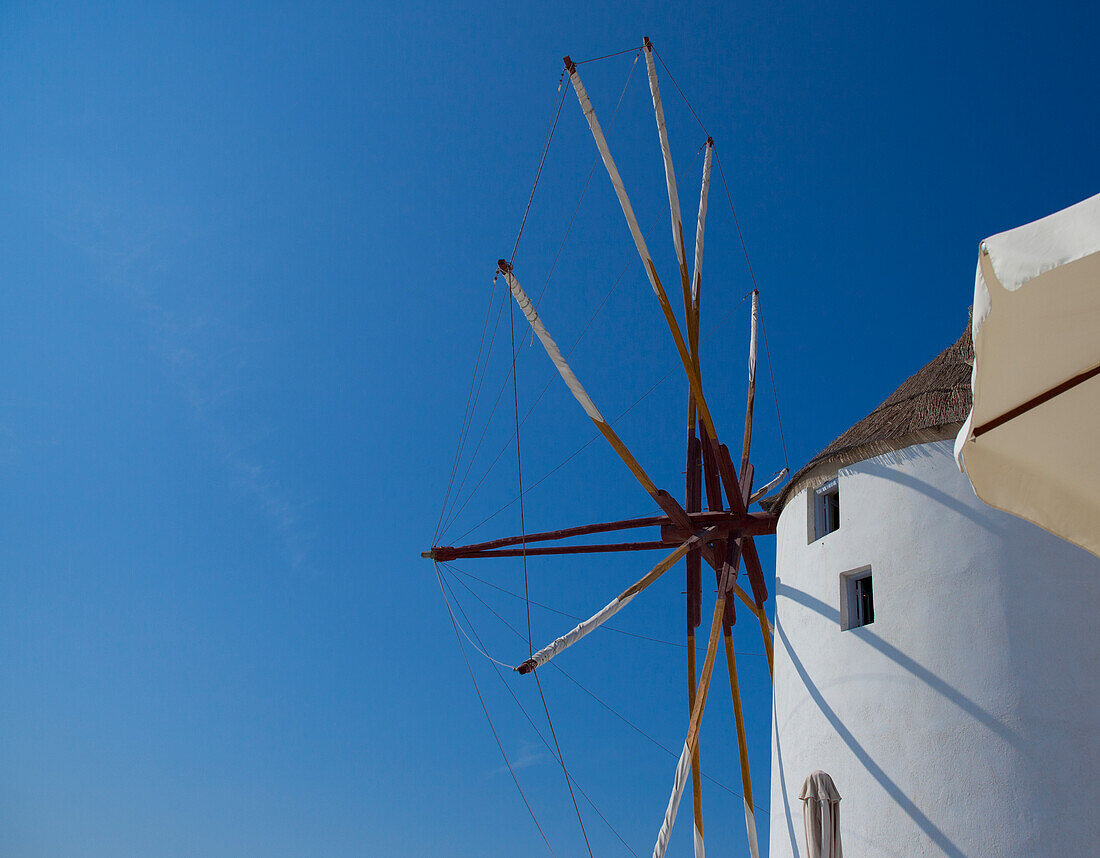 Windmühle und ein weißes Gebäude vor blauem Himmel; Oia, Griechenland