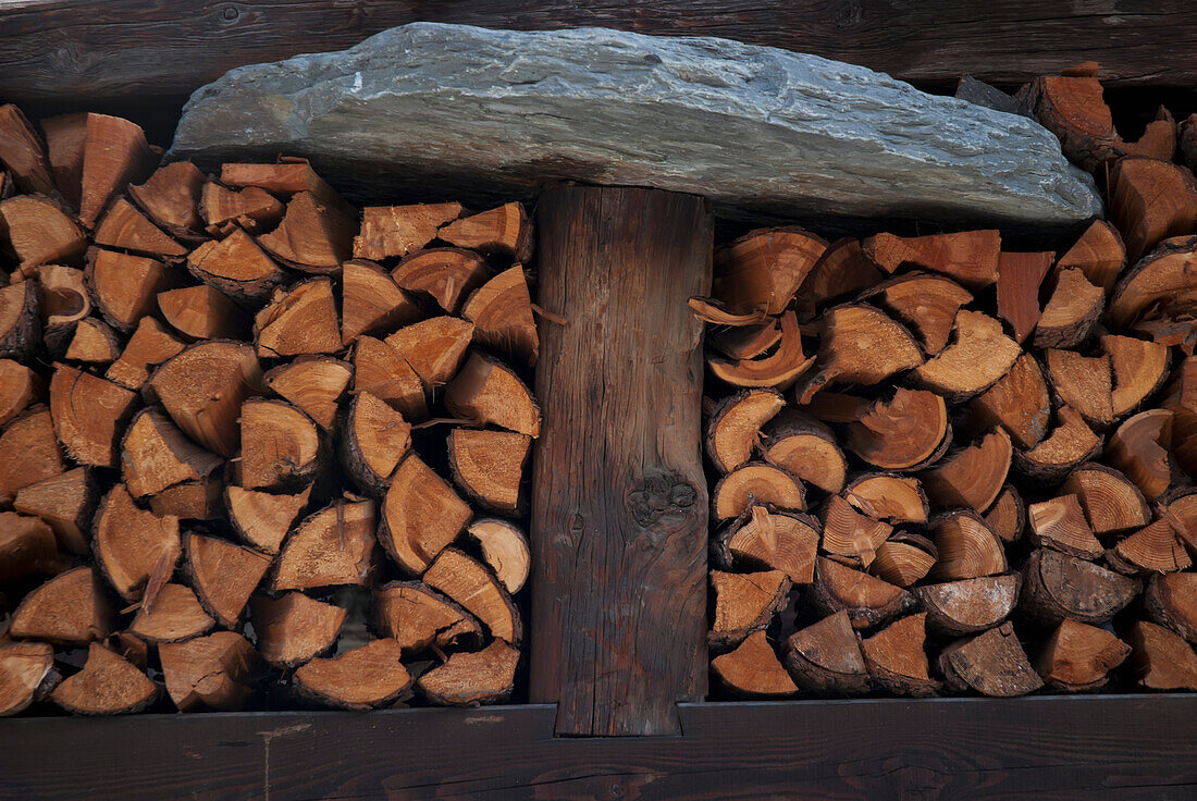 Runder Stein auf einer Holzsäule mit einem Stapel geschnittenen Holzes; Zermatt, Wallis, Schweiz