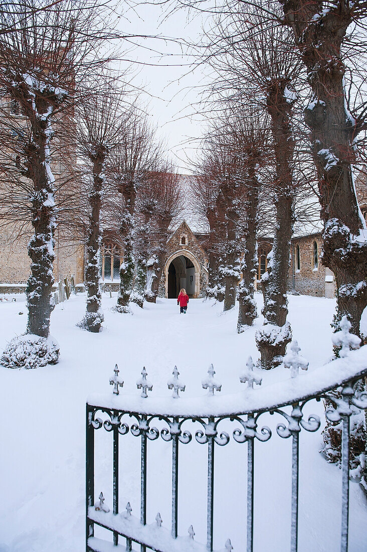 Mädchen, das im Schnee einen Weg zu einer Kirche hinaufgeht; Great wilbraham cambridgeshire england