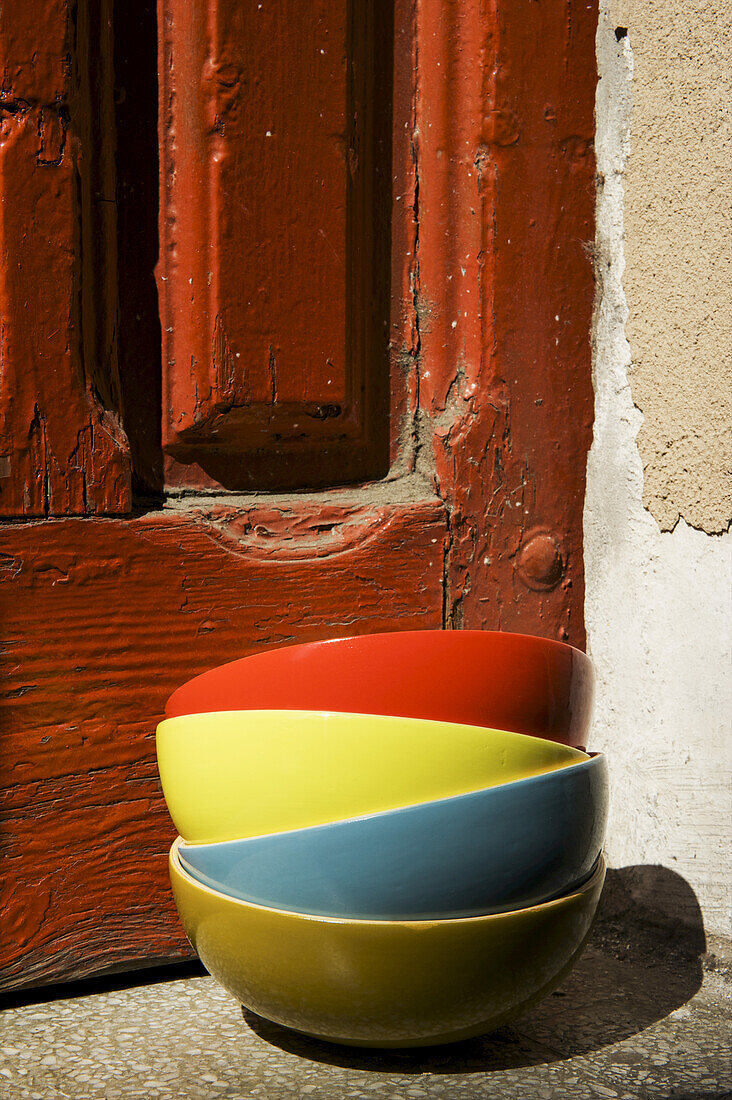 Bunte Schalen auf einem Stapel neben einer verwitterten, rot gestrichenen Holztür; Barcelona, Spanien