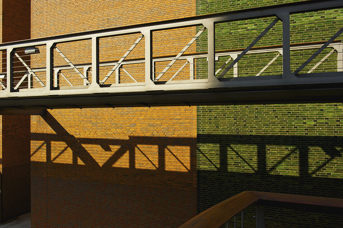 Ein erhöhter Gehweg mit einer Backsteinmauer dahinter in zwei Farben, braun und grün; Hamburg, Deutschland