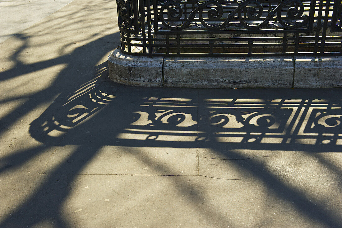 Geschmücktes Geländer und sein Schatten auf dem Betonweg; Paris, Frankreich