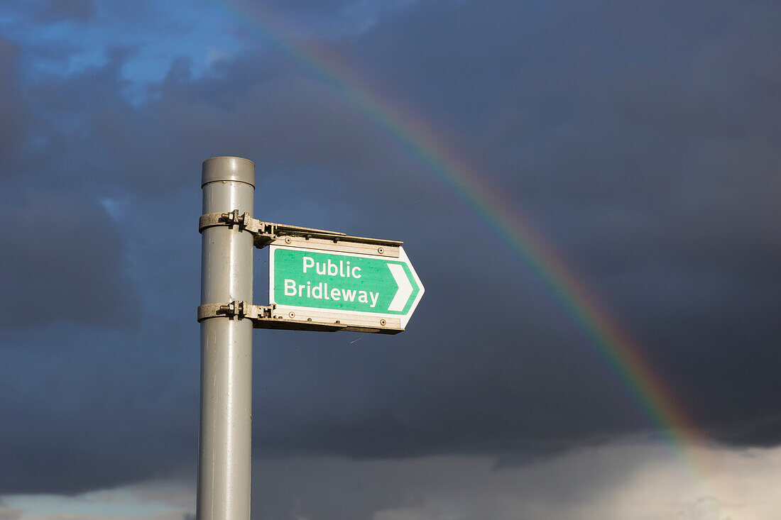 Ein Regenbogen durch die Sturmwolken und ein Hinweisschild auf einen öffentlichen Reitweg; Hertfordshire, England