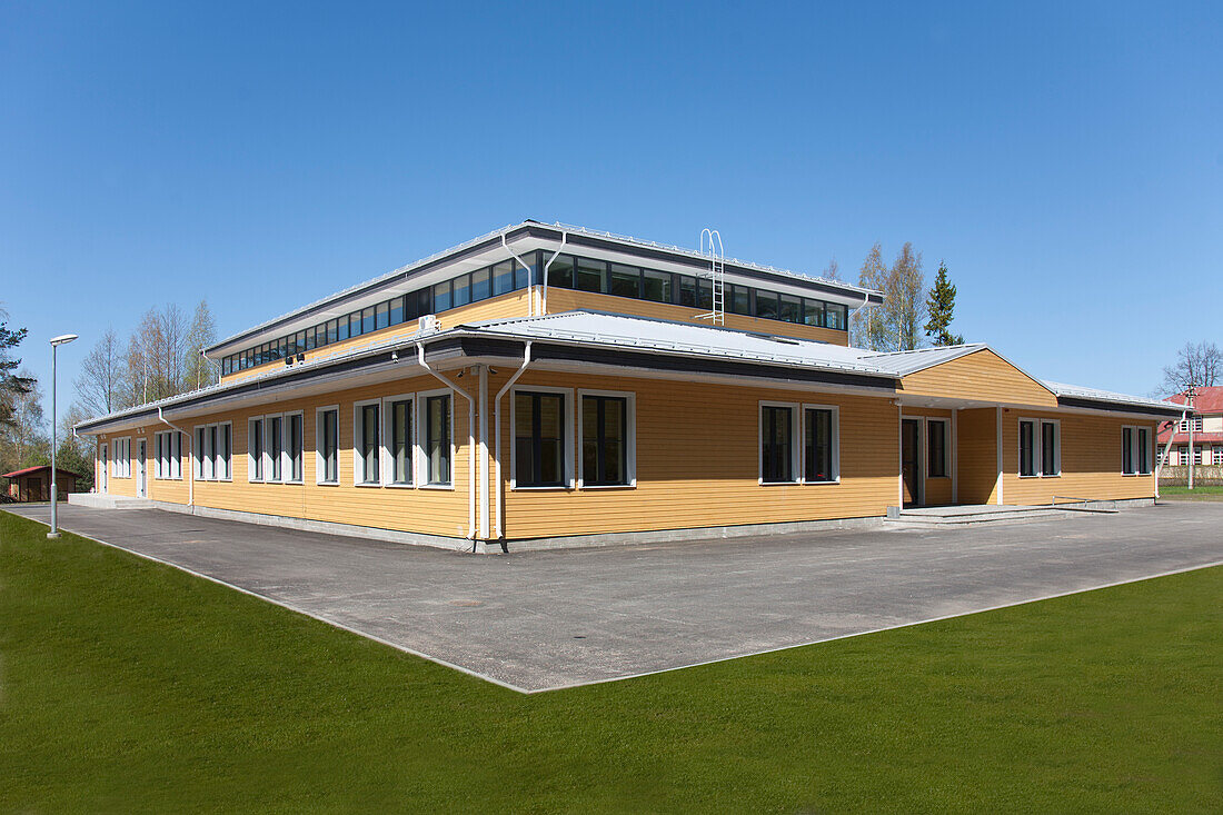 Das Äußere eines modernen Schulgebäudes, ein einstöckiges Gebäude mit Fenstern und einem Spielplatz mit Rasenfläche. 