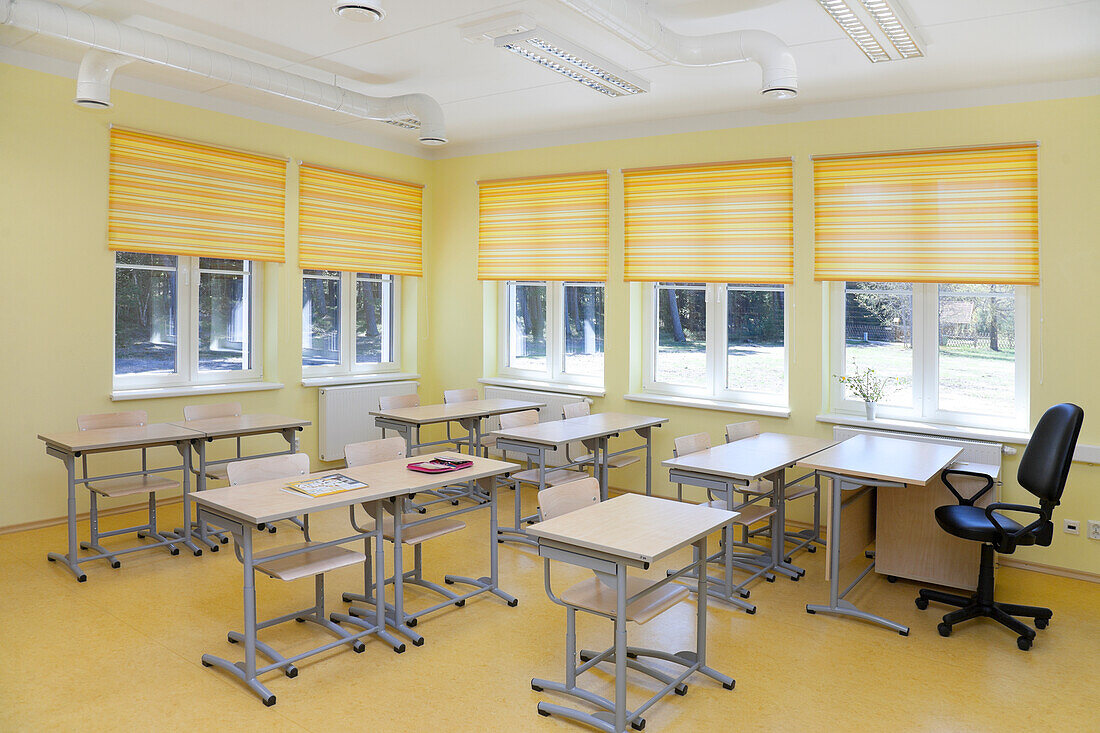 Ein Schulklassenzimmer mit Tischen und Stühlen und gelben Fensterläden.