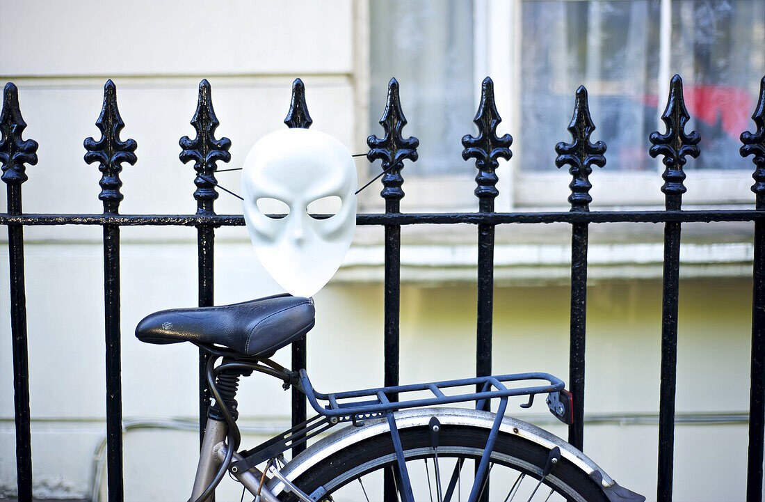 An einen Metallzaun gelehntes Fahrrad mit einer weißen Maske, Notting Hill; London, England