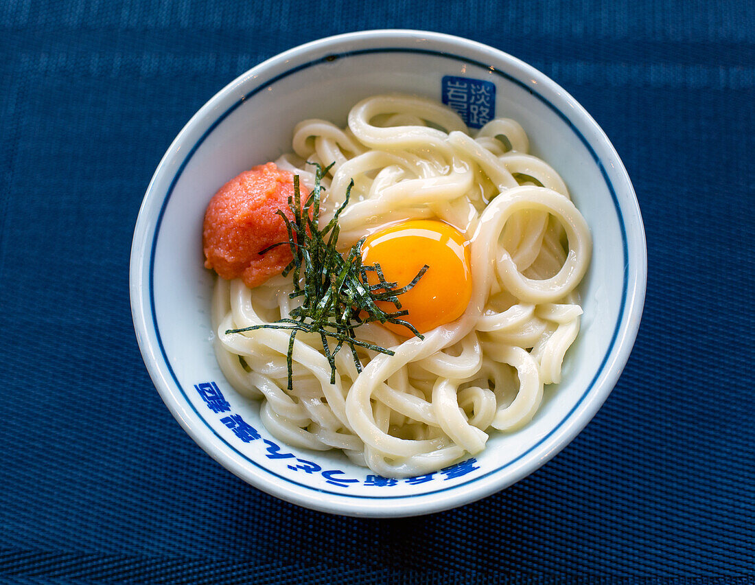 Ein Gericht aus Nudeln, Gemüse und Fisch mit einem gelben Eigelb. 