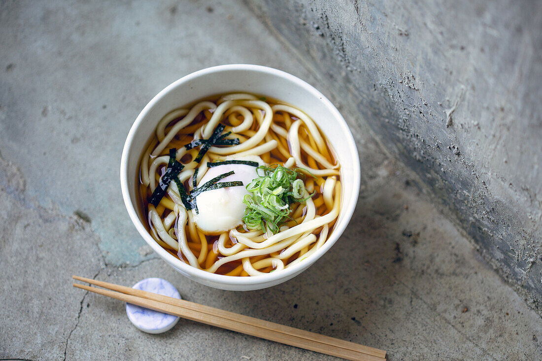 A bowl of noodles, vegetables and broth and a set of chopsticks. 