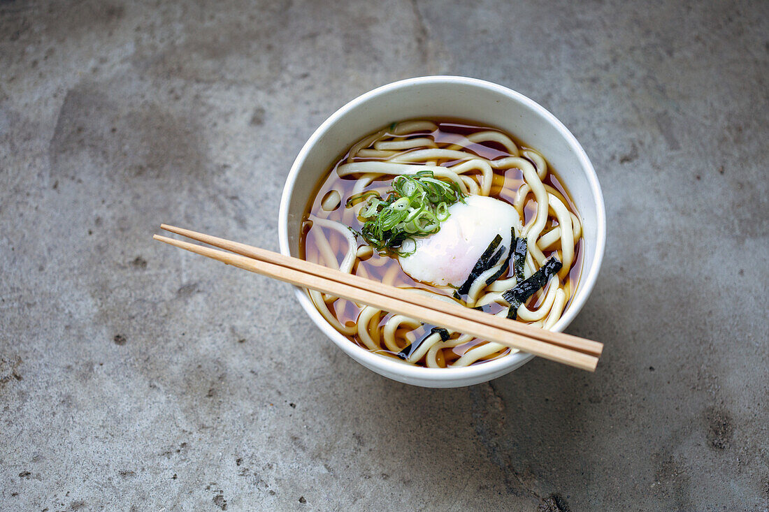 A bowl of noodles, vegetables and broth and a set of chopsticks. 