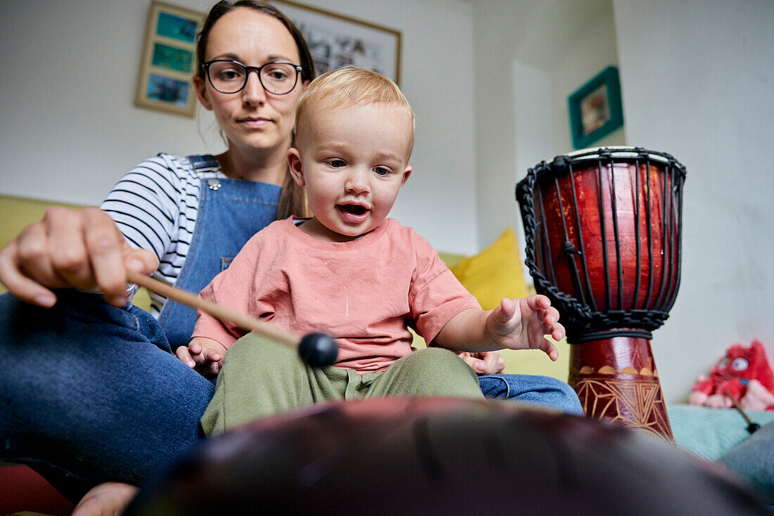 Mutter und Kleinkind spielen drinnen zusammen ein Musikinstrument