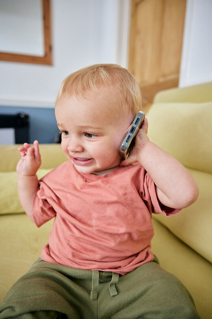 Toddler holding smart phone with animated expression indoors