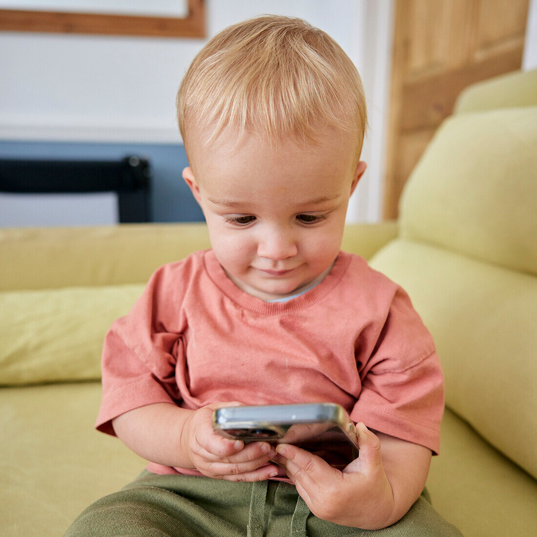 Toddler holding smart phone with animated expression indoors