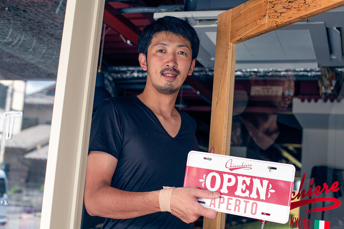 Man hanging up an Open sign on a restaurant door. Dual language, Italian and English. 