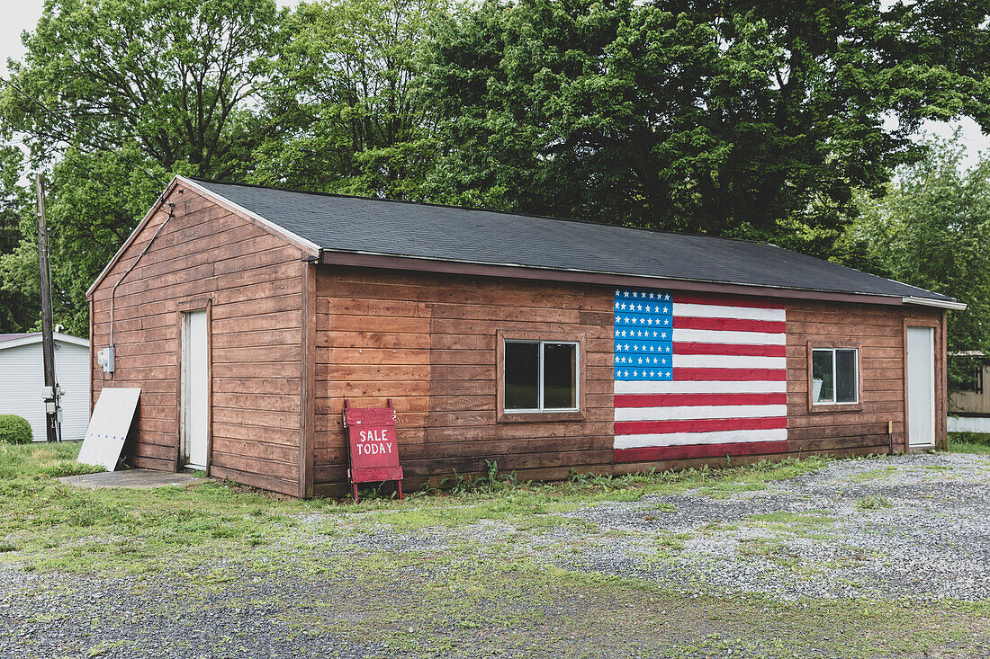 A Sale Today Eine Tafel und eine amerikanische Flagge an einem leeren Gebäude auf einer Straße in einer Kleinstadt.