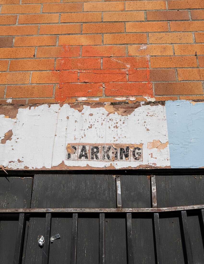 An old PARKING sign on a building wall. 