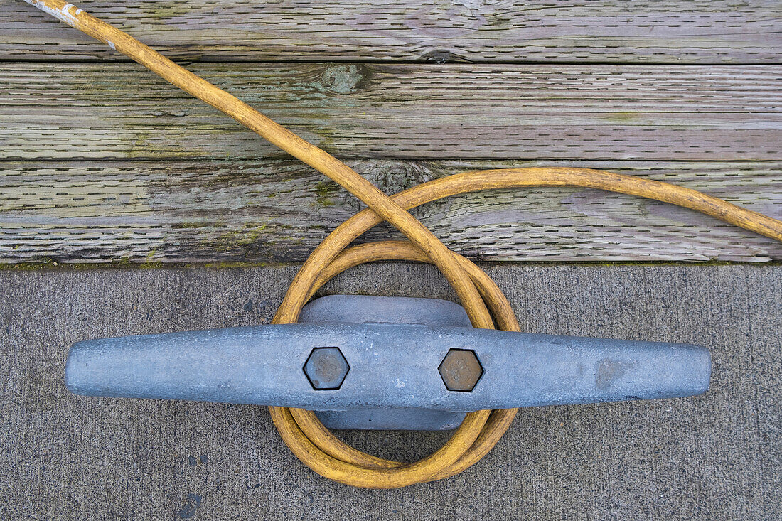 A power cable wrapped around a metal nautical cleat on the dock, quayside