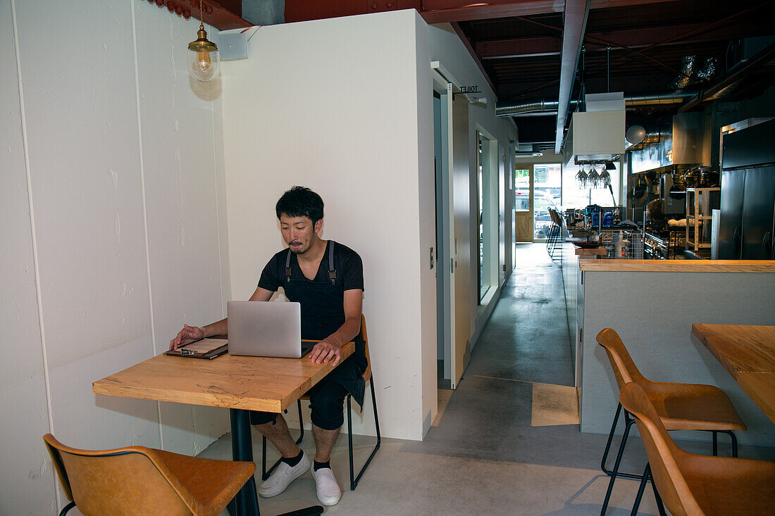 A man seated at a table using a laptop computer, owner and manager of a small restaurant. 