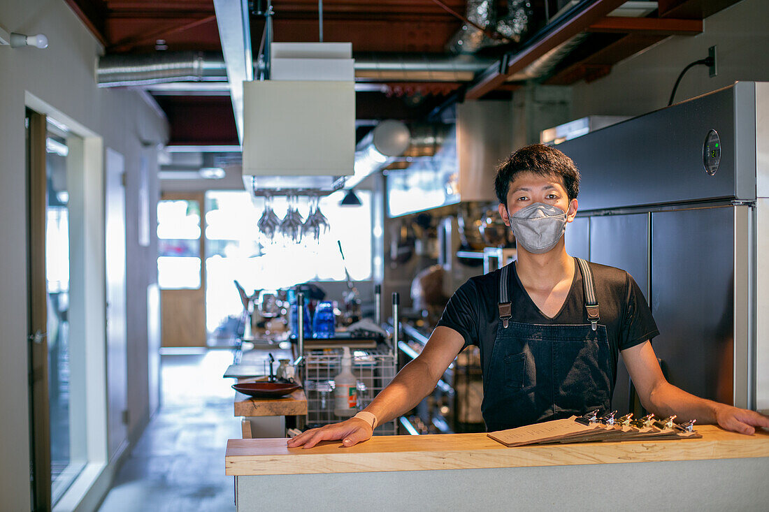 Ein Mann mit einer Gesichtsmaske an der Theke einer Restaurantküche, der Besitzer oder Manager. 