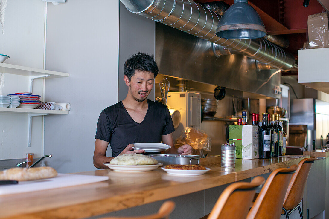 Ein Koch, der in einem Restaurant arbeitet, am Pass, der die Teller mit den Speisen für den Service vorbereitet, 