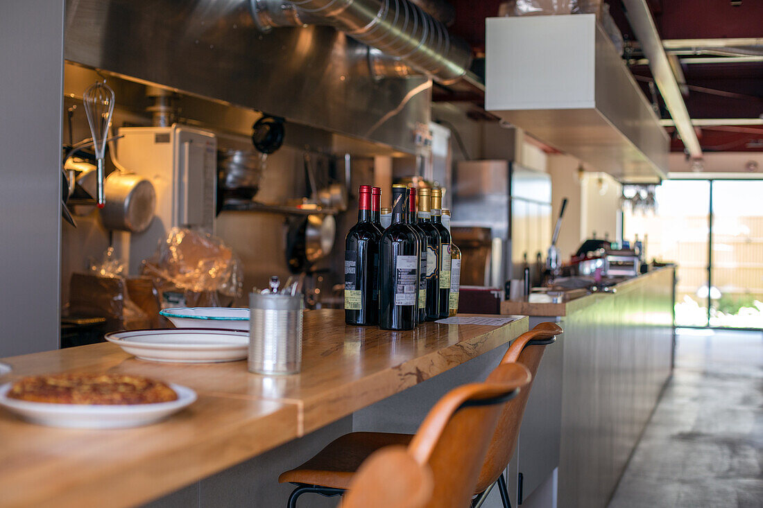 A restaurant kitchen and service counter, bottles of red wine. 