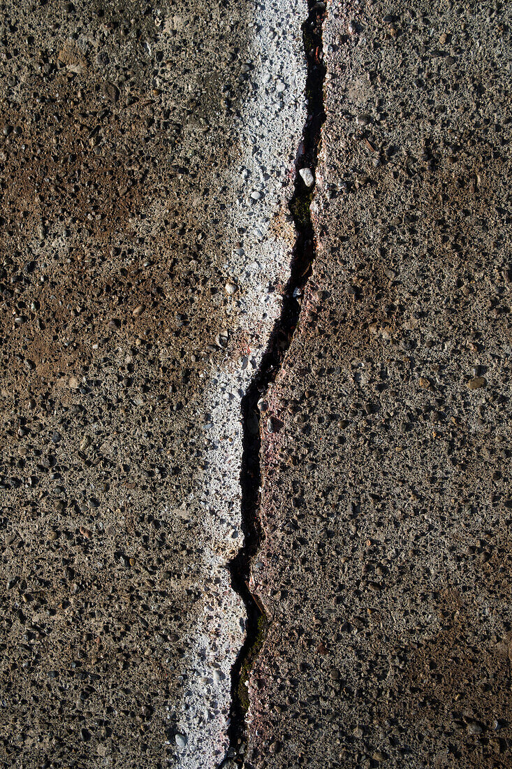 A crack on painted concrete sidewalk.