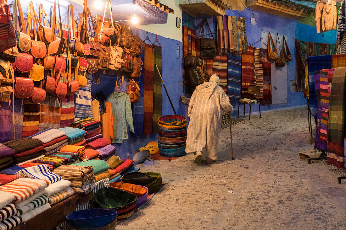 Marokko. Ein älterer Mann geht in einer Straße in der blauen Stadt Chefchaouen an Touristenläden vorbei.