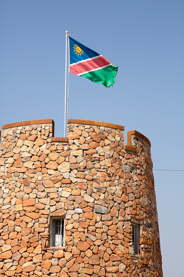 Afrika, Namibia, Etoscha-Nationalpark. Die namibische Flagge weht über dem Ziegelturm am Parkeingang