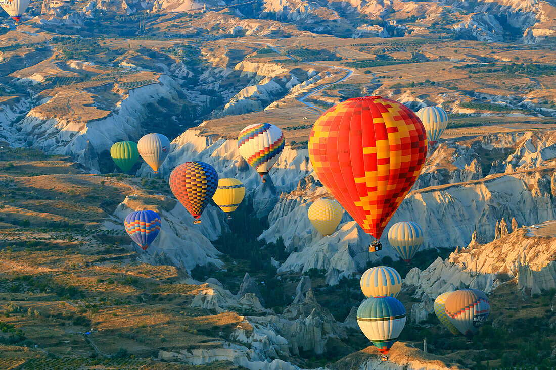 Türkei, Anatolien, Kappadokien, Goreme. Heißluftballons fliegen über Felsformationen und Feldlandschaften im Roten Tal, Goreme-Nationalpark, UNESCO-Welterbe.