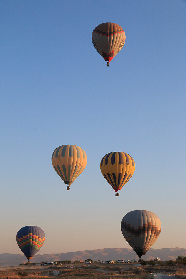Turkey, Anatolia, Cappadocia, Goreme. Hot air balloons flying above rock formations and field landscapes in the Goreme National Park, UNESCO World Heritage Site.