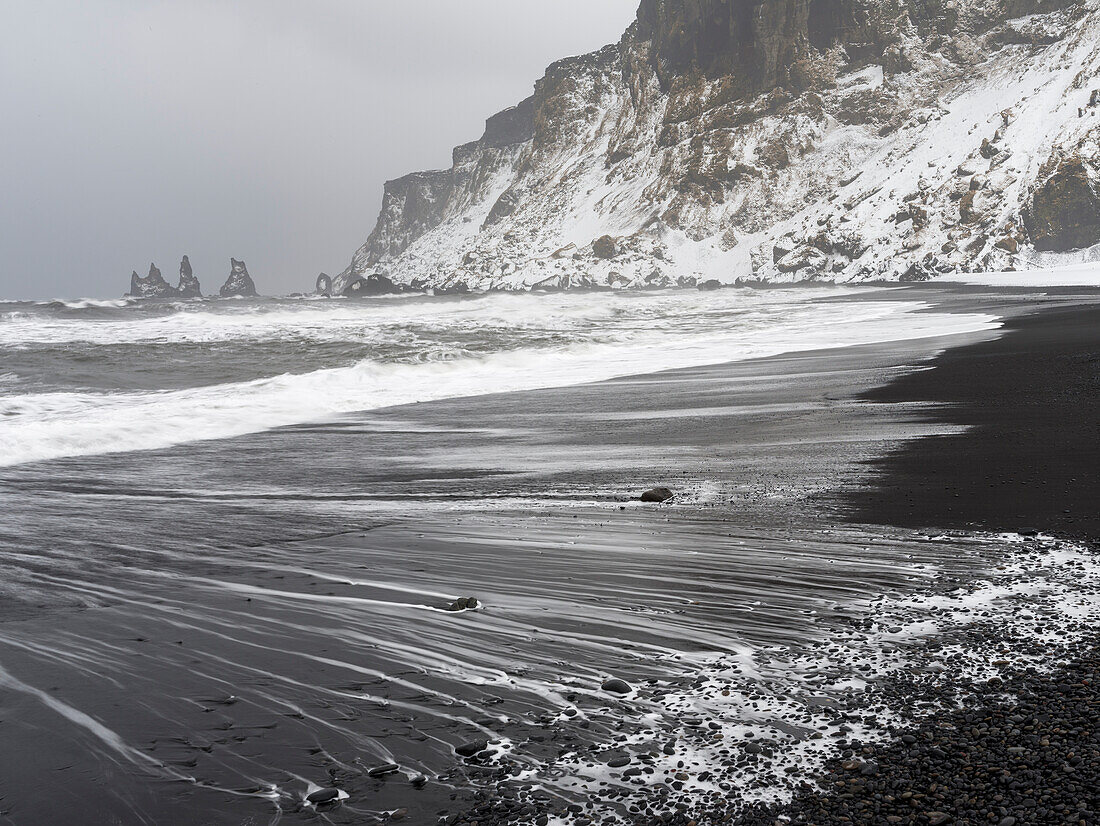 Die Küste des Nordatlantiks bei Vik y Myrdal im Winter. Strand nach einem Schneesturm mit den Reynisdrangar genannten Meeresstapeln. Skandinavien, Island