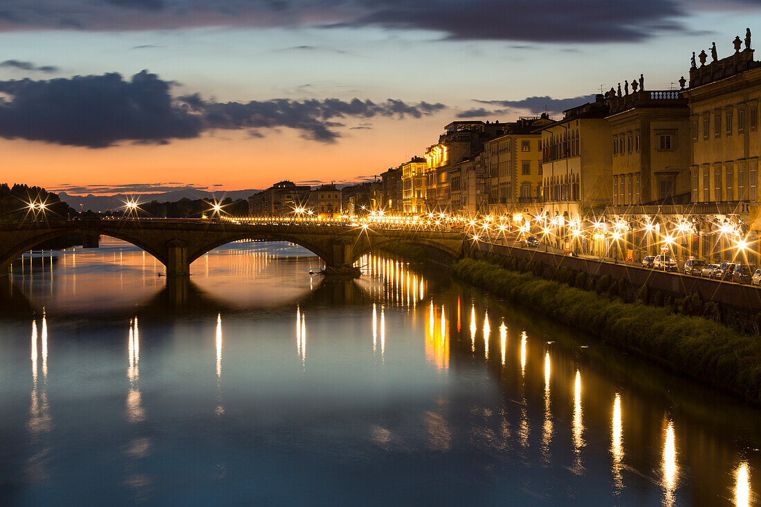 Italien, Florenz. Bei Einbruch der Dämmerung beleuchten die Straßenlaternen der Stadt die Straßen und Brücken am Flussufer.
