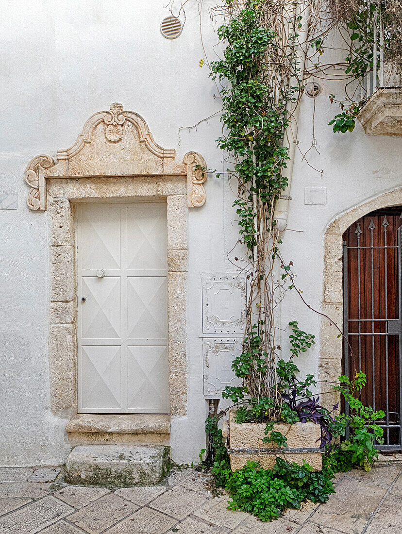 Italien, Apulien, Brindisi, Itria-Tal, Ostuni. Kunstvolle Schnitzereien rund um die Türen und Topfpflanzen in den Gassen und engen Straßen der weißen Stadt Ostuni.