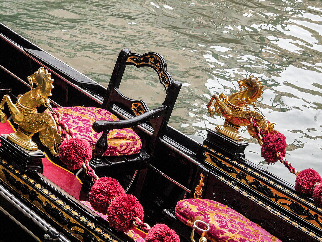 Venedig, Italien. Gondelinterieur mit goldener Pferdeschlange, Samtkissen, schwarzem Stuhl, auf einem Kanal