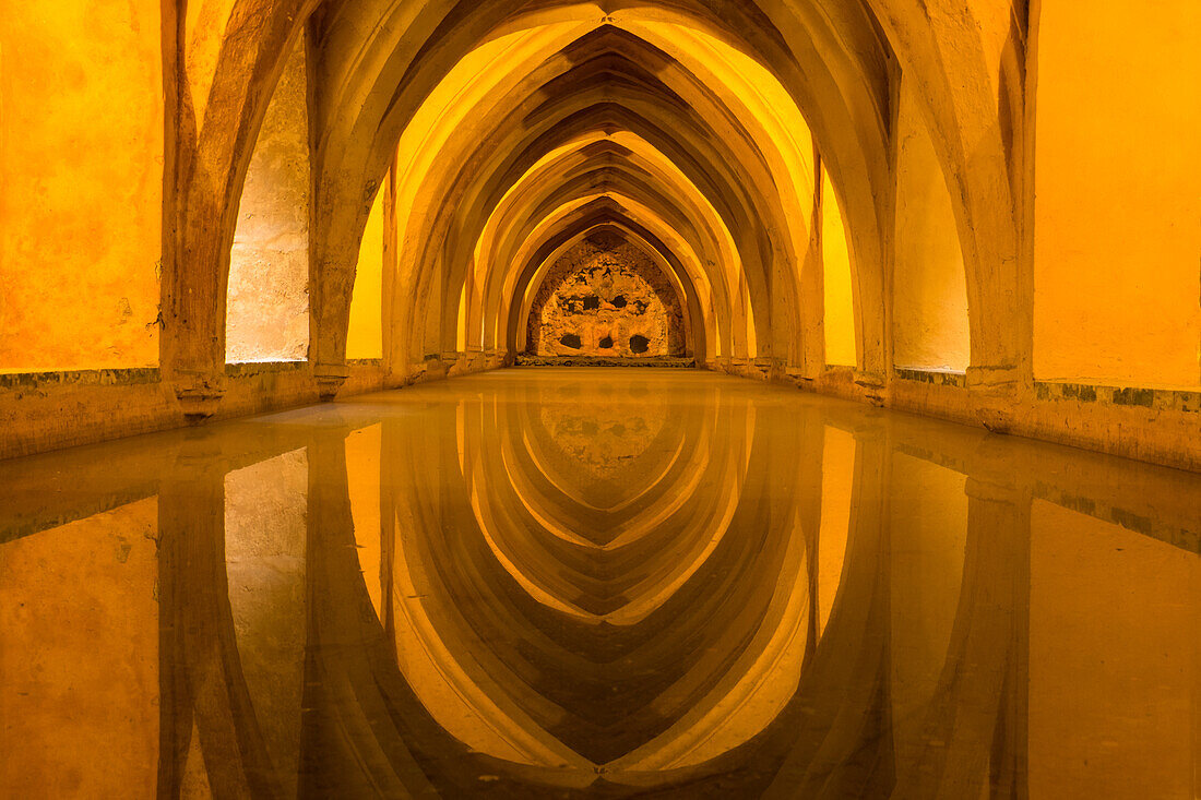 Spanien, Andalusien, Sevilla. Die sich wiederholenden Bögen im Inneren der Bäder spiegeln sich im ruhigen Wasser des Alcazar.
