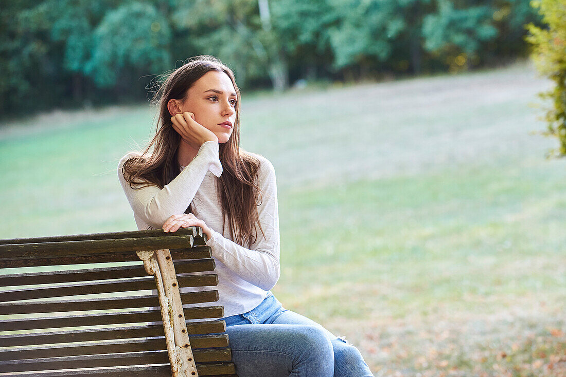 Nachdenkliche junge Frau sitzt auf einer Bank in einem Park