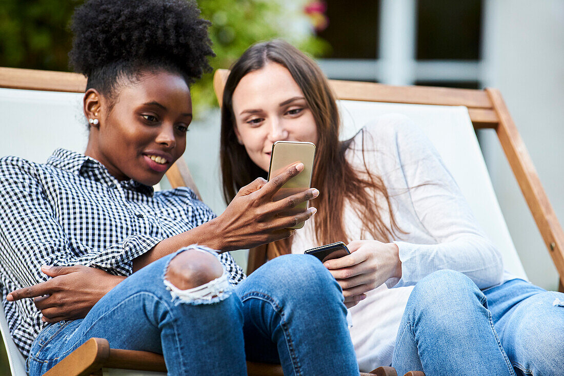 Smiling young friends using smartphones in park