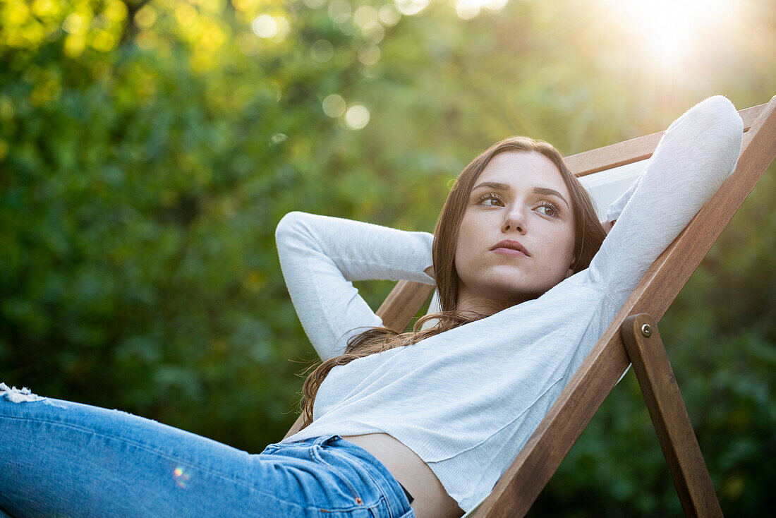 Thoughtful young woman with hands behind head leaning on chair