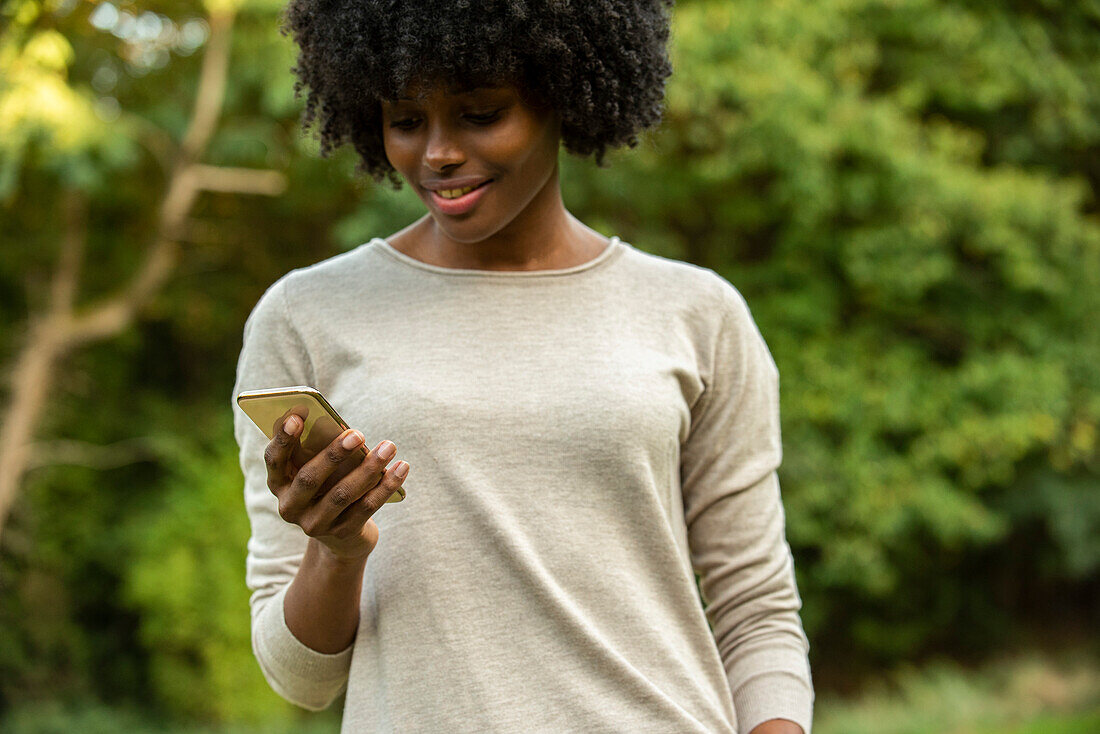Smiling young woman using smart phone in park