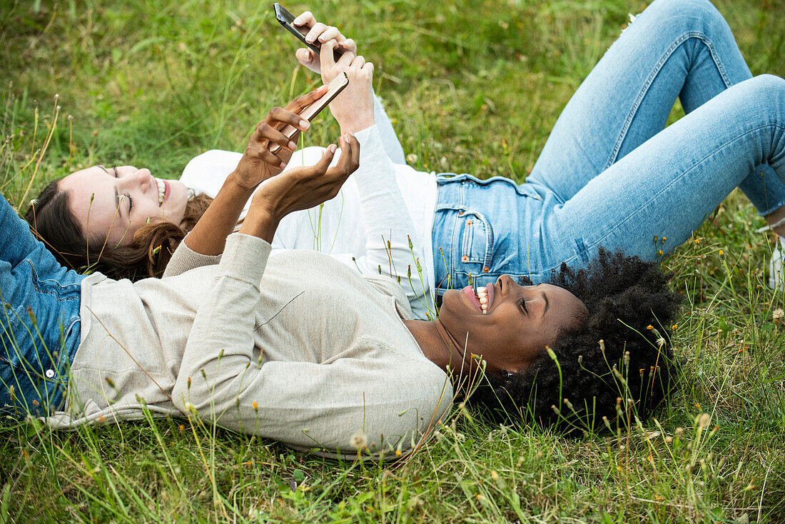 Young female friends lying on grass while using smart phone in park
