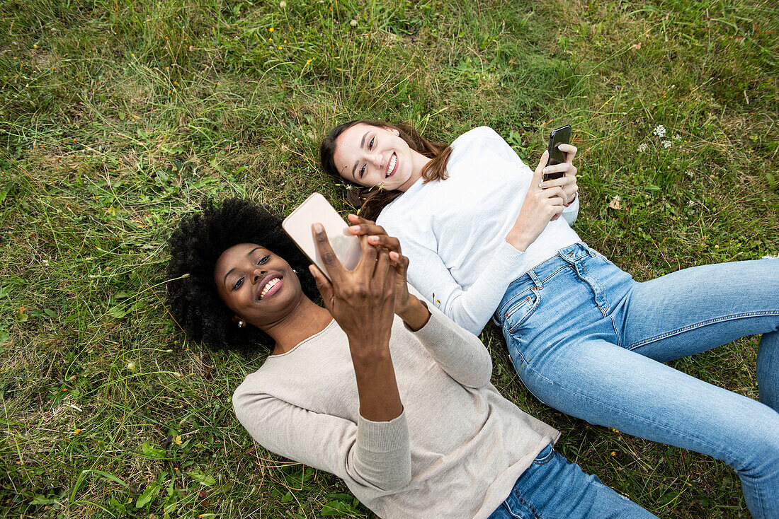 Young female friends lying on grass while using smart phone in park