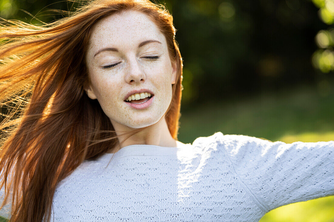 Close-up of smiling young woman with eyes closed in park