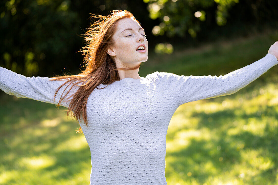 Young woman with eyes closed stretching her arms in park