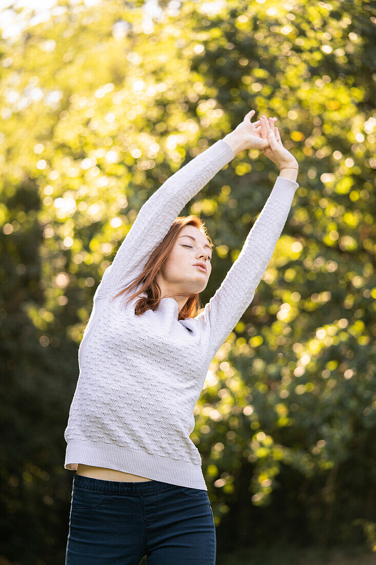 Young woman with eyes closed stretching her arms in park