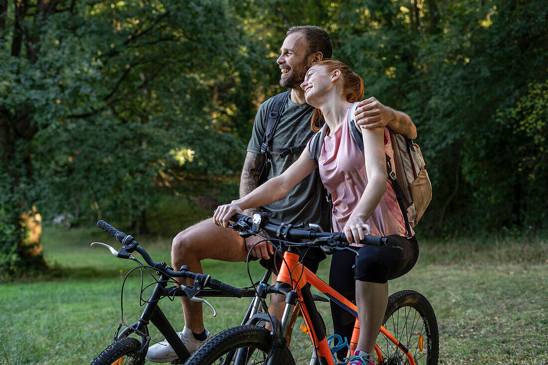 Lächelndes junges Paar auf Fahrrädern im Wald sitzend