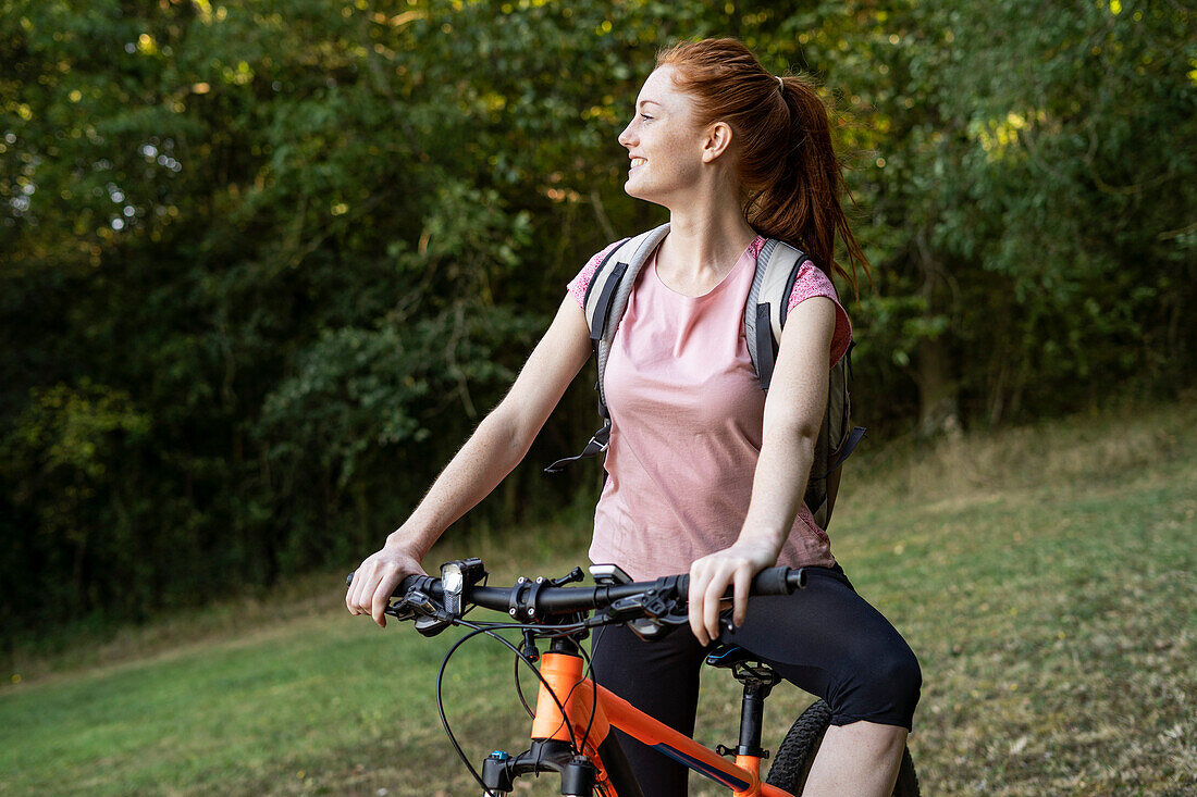 Lächelnde junge Frau auf einem Fahrrad im Wald sitzend