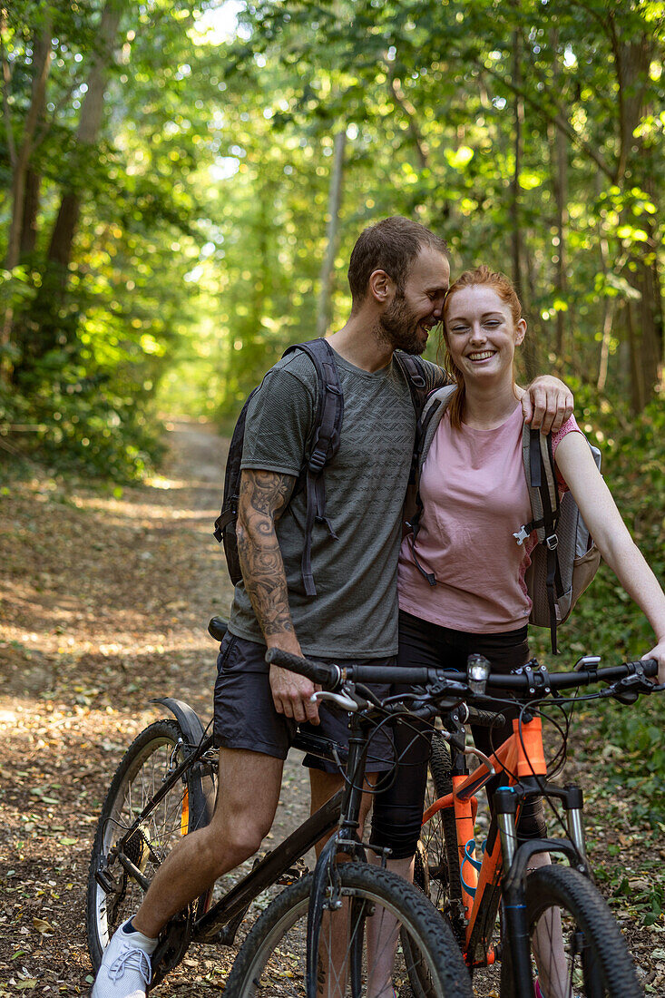 Smiling young couple standing with bicycles in forest